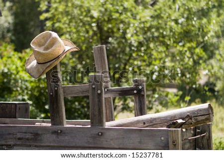 A straw cowboy hat hanging from a post on an old wood wagon.