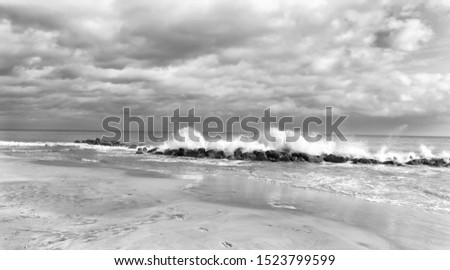 Black and white photo of waves crashing on some rocky barrier.