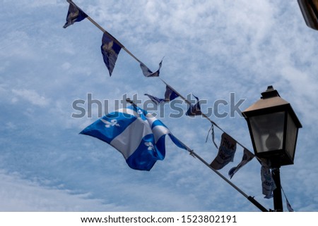 Flag of Quebec and banner with near a lamppost.The flag of Quebec is composed of a large white cross and four rectangles of blue each adorned with a white lily