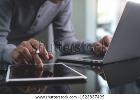 Casual business man, website designer touching on digital tablet screen and working on laptop computer, connecting internet network on table in modern office, close up. E-business, Online working 