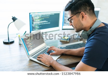 Side view of attractive Hispanic developer programming software using computer while working from home Royalty-Free Stock Photo #1523847986