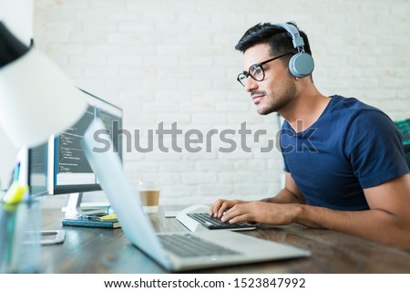 Handsome young male software developer programming codes while working from home Royalty-Free Stock Photo #1523847992