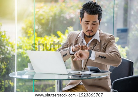 young business man checking time on smart watch while using laptop