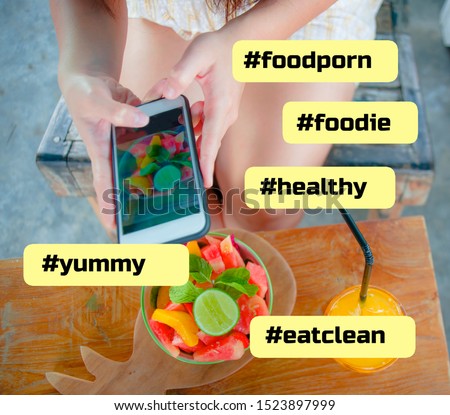 close up female hand with mobile phone screen taking picture of fruit salad and orange juice for sharing on internet social media app in healthy nutrition lifestyle composed with foodie hashtags