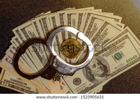 Handcuffs on hundred dollar bills and a gold bitcoin coin. Top view