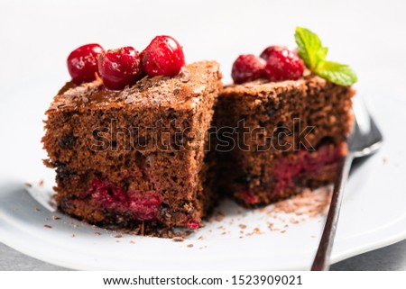 Cherry chocolate cake cut into squares on plate, closeup view. Isolated on white. Sweet chocolate dessert cake