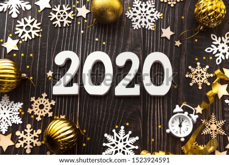 Happy New Year 2020 flatlay composition. Christmas toys and white snowflakes on a black wooden background