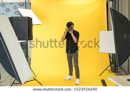 Young Professional photographer is taking picture in modern studio with photo studio background.