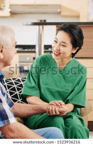 Pretty positive medical nurse holding hand of senior patient she is visiting weekly at home
