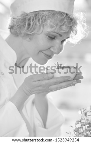 Black and white photo of mature chef smelling mints in bowl