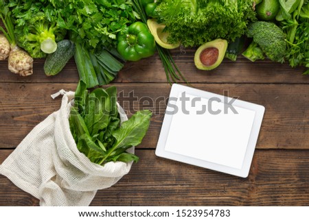 Order food online Tablet with blank screen for your text message or design on wooden background with fresh green vegetables and fabric bag