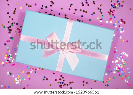 Beautiful blue gift box with pink atlas ribbon on purple pink background with sparkling stars, festive concept