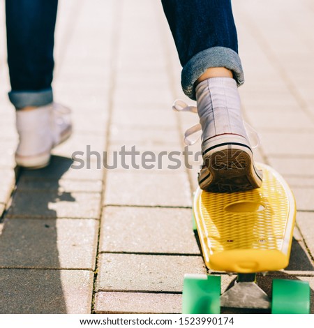 Close up of slim lady in jeans and white sneakers ready to ride her penny board skateboard in sunset light. Modern urban hipster girl have fun. Good sunny summer day for skateboarding and have fun.