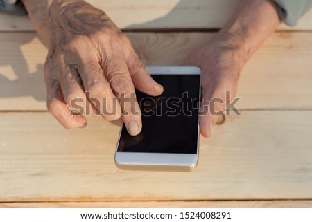 Hands of an elderly man holding and using a phone. The concept of teaching new technologies to older people, communication with the older generation. Image. Royalty-Free Stock Photo #1524008291