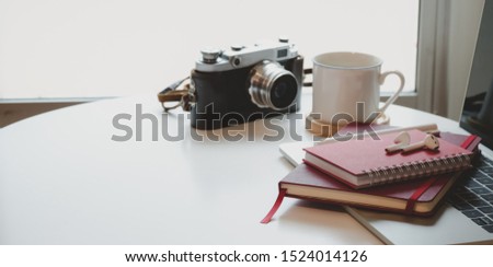 Cropped shot minimal workplace with notebook and vintage camera on white wooden table near the windows 