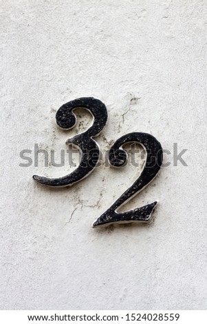 House number 32 on a white plaster wall as metal digits