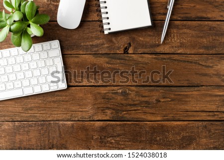Office desktop with computer keyboard, mouse, notebook, pen and green plant on wooden table. Business background