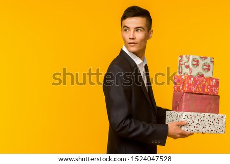 Handsome asian businessman holding gift box over yellow background - image