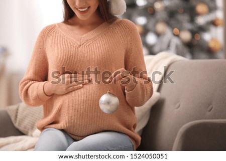 Happy pregnant woman with Christmas ball in living room, closeup. Expecting baby