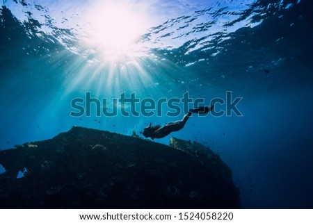 Free diver girl in pink swimwear with fins swimming underwater at wreck ship. Freediving in the ocean
