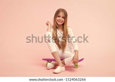 Enjoying vibes on penny board. Cute little child sitting on penny board deck on pink background. Adorable girl skater with violet penny board. Small skateboarder with penny skateboard.