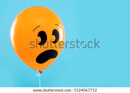 Orange balloon with drawing of scared face on blue background, space for text. Halloween party