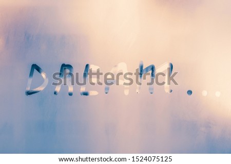 Word - dream... Abstract background with drops of water. Inscription on foggy window. Handwritten text on wet glass.
