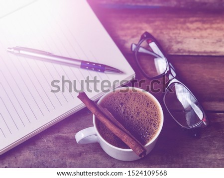 White mugs has Cappuccino coffee,Eyeglasses on empty book on wood table top,rustic still life,soft dark tone,dimly light,with lens flare,free space for your text. Concept of Relaxation in Coffee time.