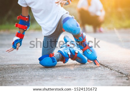 Cute asian child girl riding on roller skates and fall down in the park