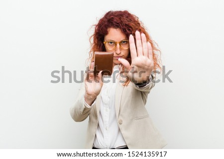 Young caucasian redhead woman holding a wallet standing with outstretched hand showing stop sign, preventing you.