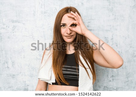 Young fitness woman showing okay sign over eyes