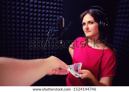 Moment of transfer of euros from hand to hand for the singer behind the microphone. A young woman smiles getting money for work in a recording studio.