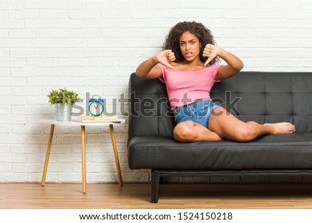Young african american woman sitting on the sofa showing thumb down and expressing dislike.