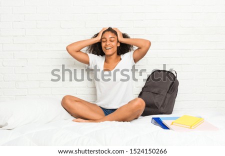Young african american student woman on the bed laughs joyfully keeping hands on head. Happiness concept.