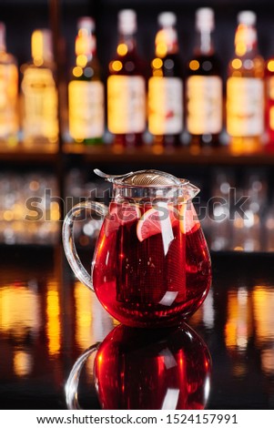 Beautiful transparent teapot with red fruit tea on a shiny dark table against the background of a blurred bar. Close-up. Space