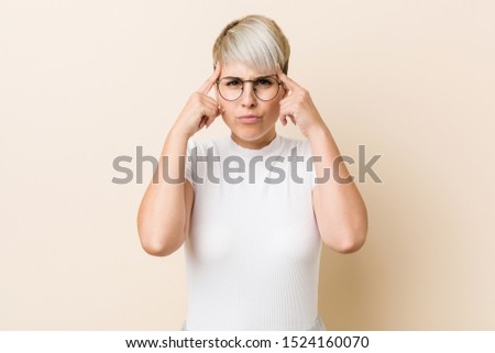 Young authentic natural woman wearing a white shirt focused on a task, keeping forefingers pointing head.