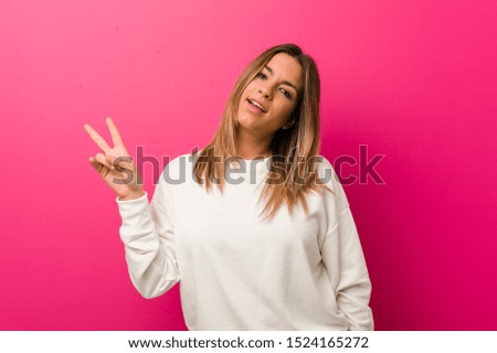 Young authentic charismatic real people woman against a wall joyful and carefree showing a peace symbol with fingers.