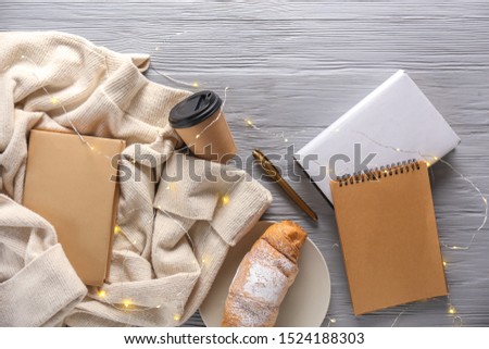 Notebooks with cup of coffee, croissant, sweater and garland on grey wooden background