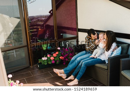 Portrait of young smiling family playing with son on the patio. Happy family, parenthood and people concept - mom, dad with baby boy near home. Spends time together on the terrace.
