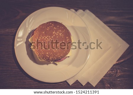 Burger with salami, cheese and cheese paste on a white plate.Wooden rustic background. Breakfast.