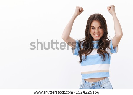 Successful cheering cute ambitious young woman lift hands, fist pump joyfully smiling toothy squinting from happiness, celebrate success, win prize lottery, stand white background dancing rejoice