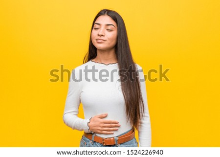 Young pretty arab woman against a yellow background touches tummy, smiles gently, eating and satisfaction concept.