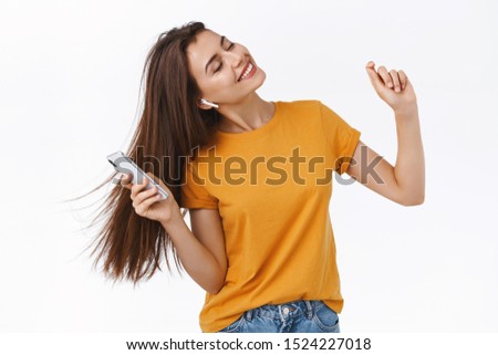 Girl whip her hair back and forth as enjoying awesome sound of wireless earphones, holding smartphone, close eyes relaxed and carefree dancing to rhythm of music, white background