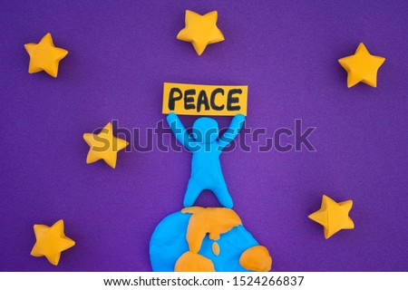 Person standing on planet Earth and holding the word Peace. Concept image. Person and planet Earth are made out of play clay (plasticine).