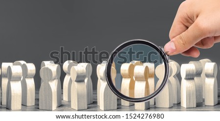 A magnifying glass looks at a crowd of wooden figures of people. society, demographic. group of citizens, rally, political movement or electorate. Customers and buyers, preferences of Population. Royalty-Free Stock Photo #1524276980