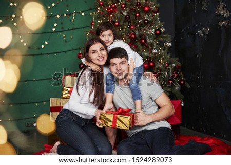 Posing for the picture. Lovely family sits near the Christmas tree with gift boxes on winter evening, enjoying the time spending together.
