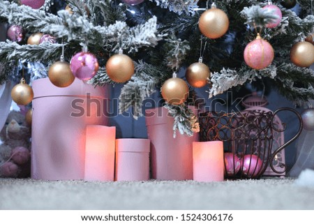 Round boxes and electric candles stand under a snowy Christmas tree on the floor. Close-up