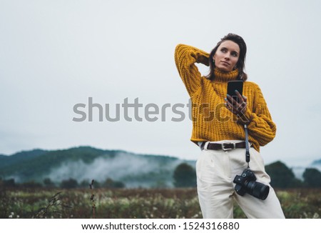 photographer girl hold in hands mobile typing message on smartphone on background landscape autumn foggy mountain, tourist shoot on photo camera using internet online gadget, hobby concept