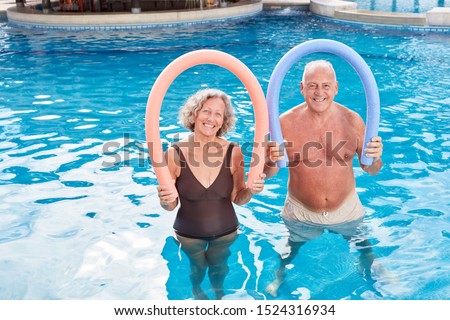 Happy seniors couple with swimming noodle in the swimming pool from the hotel