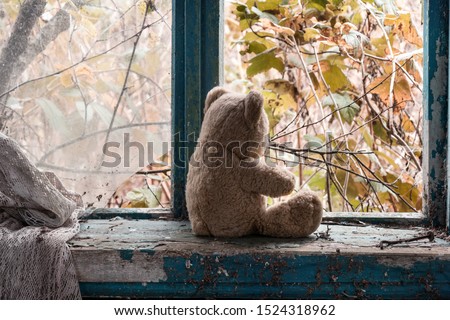 an abandoned teddy bear sits by a broken window in an abandoned house and looks at an abandoned autumn garden Royalty-Free Stock Photo #1524318962